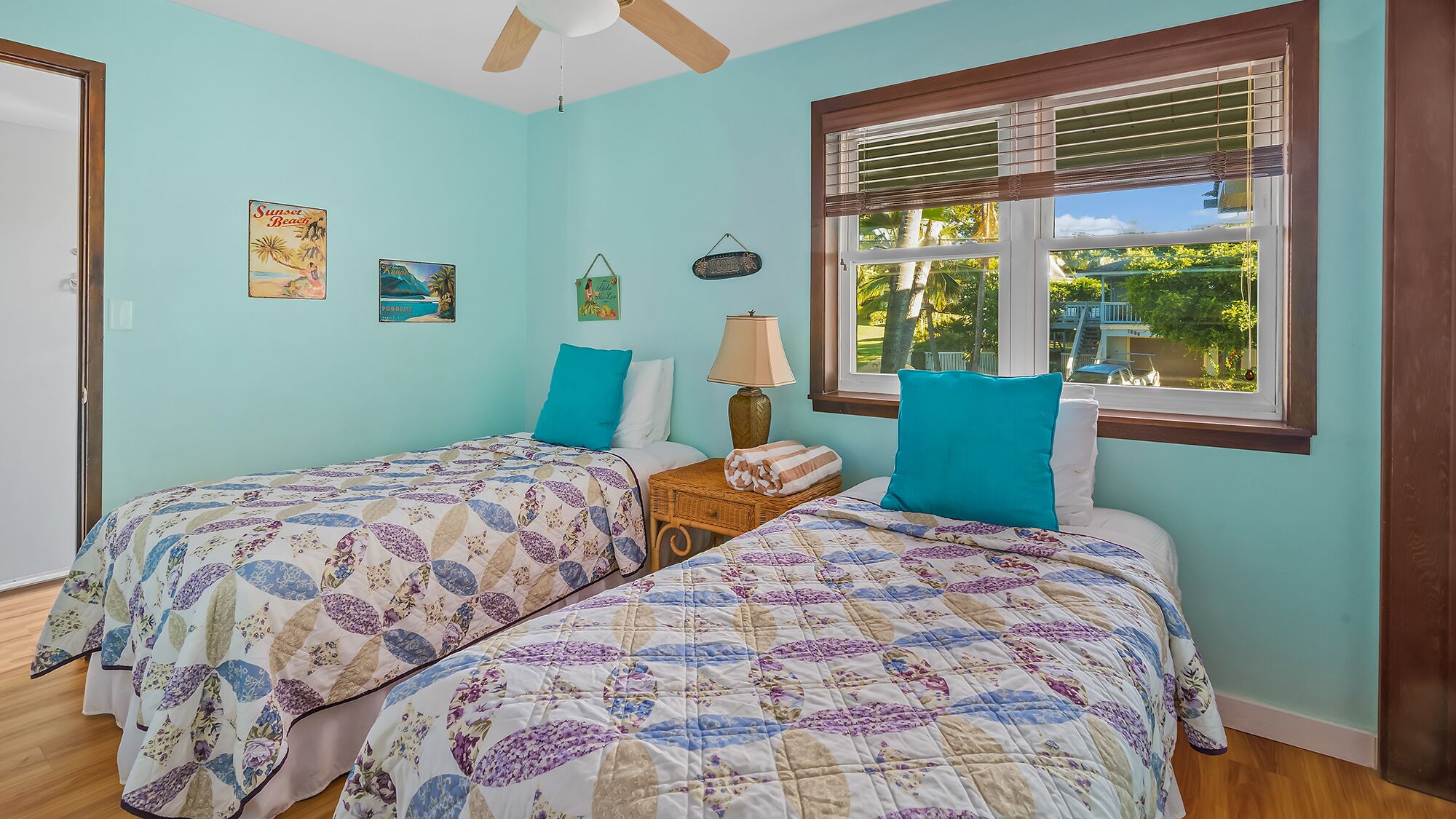 A bedroom with two beds, a window with blinds, a ceiling fan, and wall decorations.