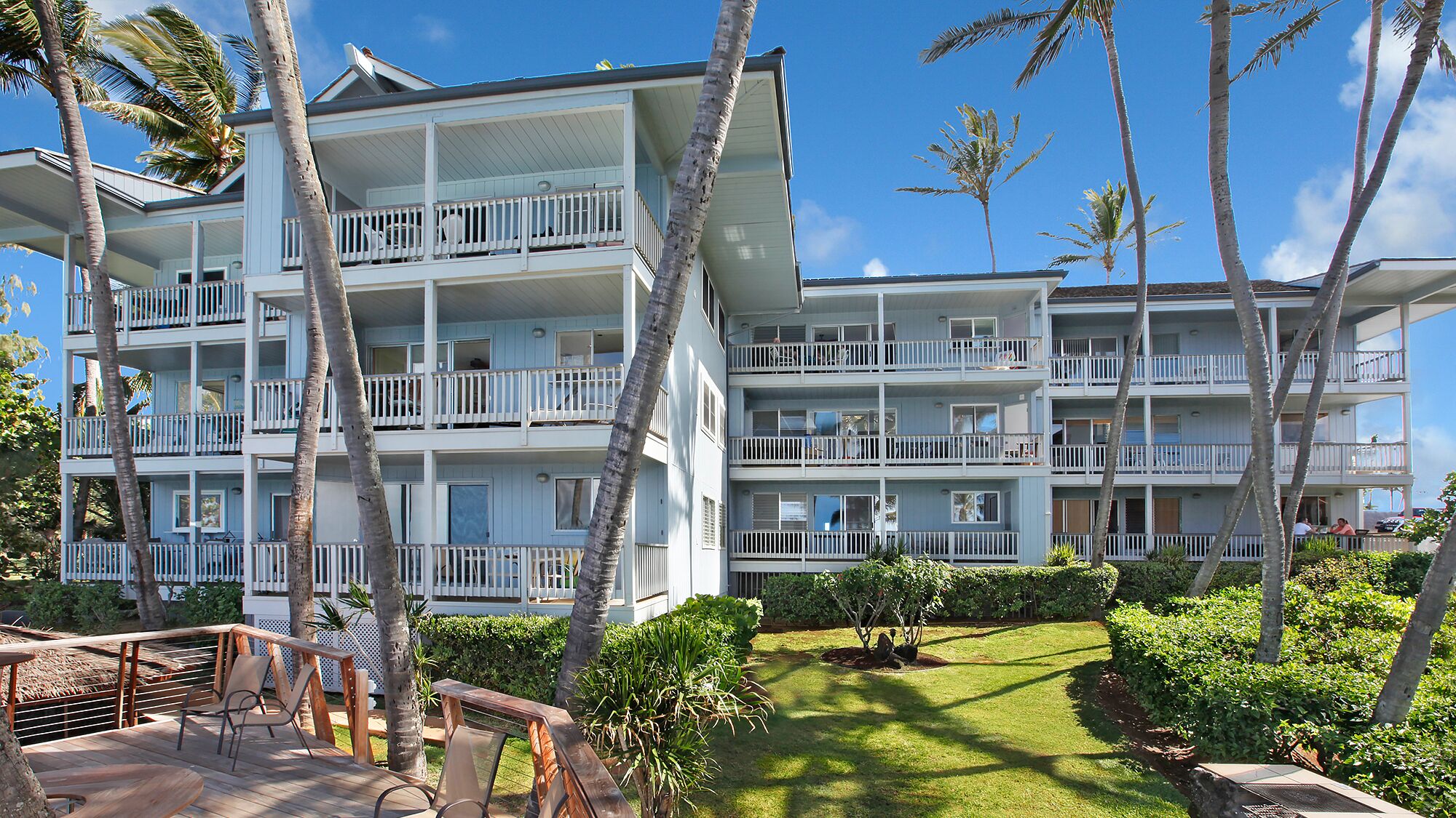 A multi-story hotel with balconies, surrounded by palm trees and a well-maintained lawn.