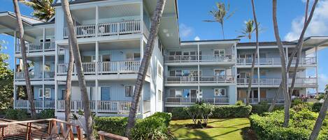 A multi-story hotel with balconies, surrounded by palm trees and a well-maintained lawn.