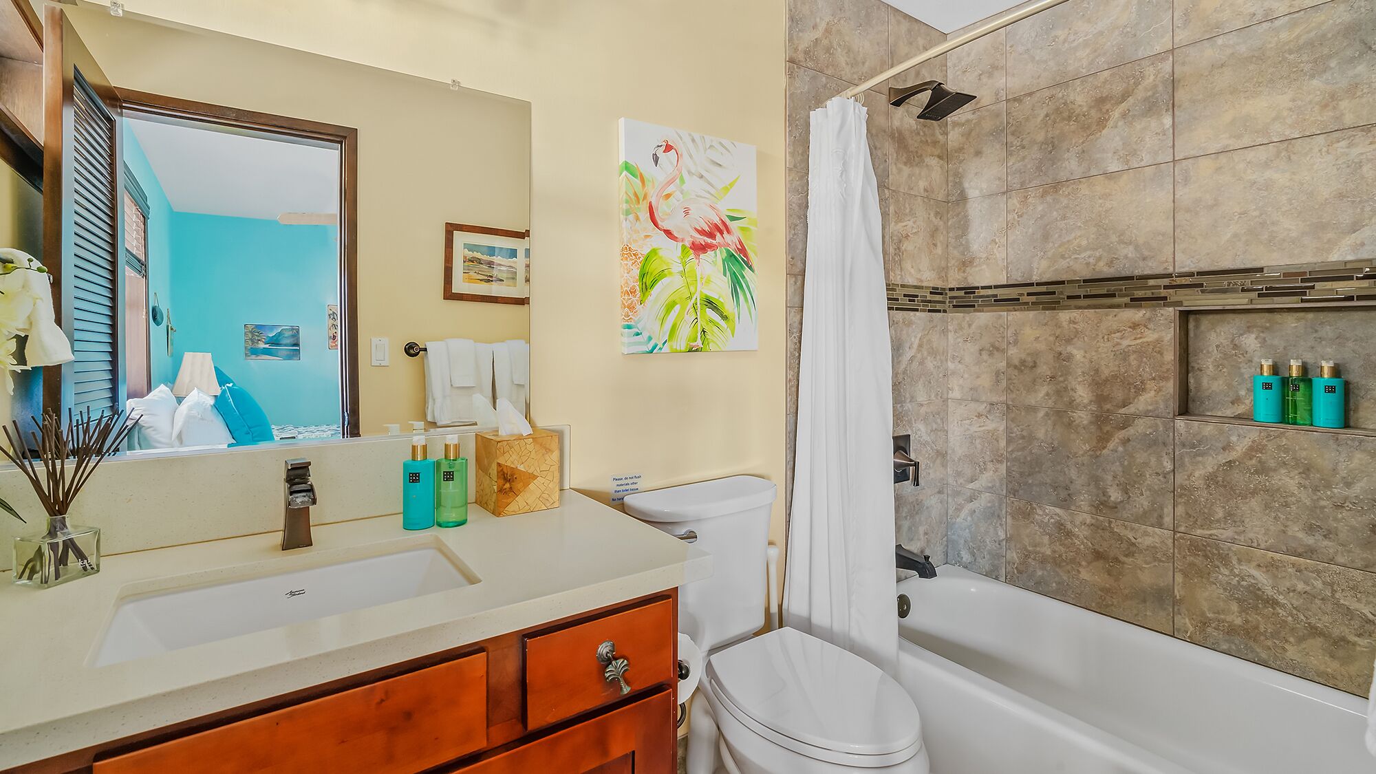 A bathroom with a sink, toilet, and bathtub. There is a shower curtain, a mirror, and a framed picture on the wall.