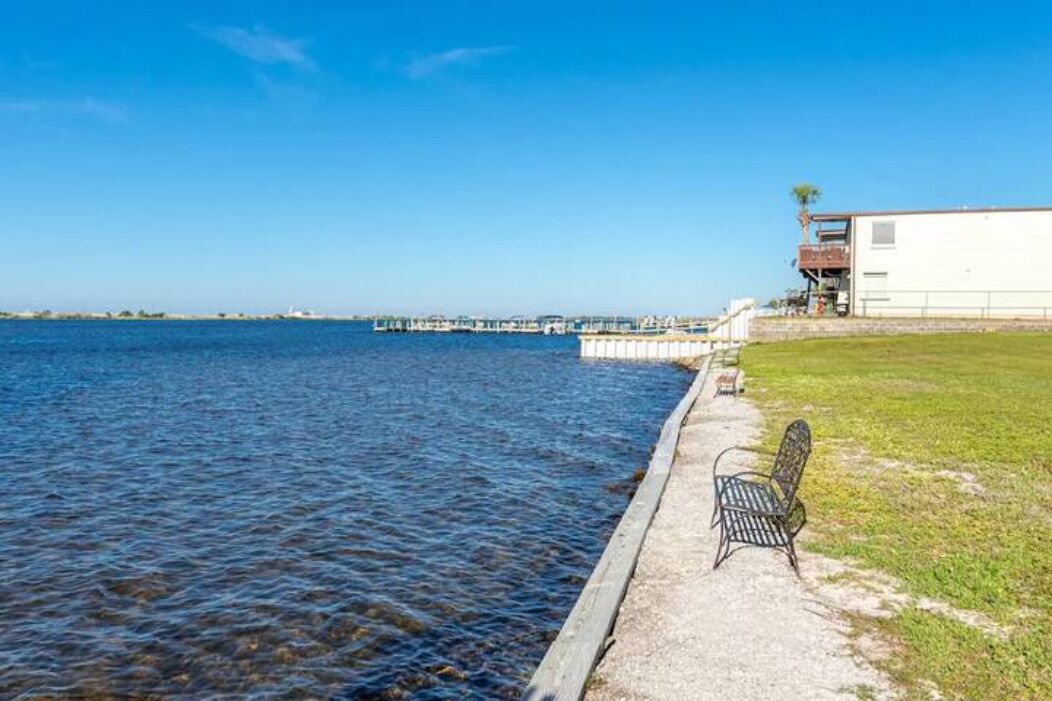 A waterfront view with a bench and a building with a balcony overlooking the water.