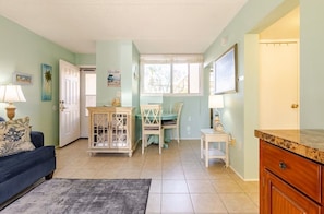 A room with a blue sofa, a wooden cabinet, a dining table with chairs, and a window with blinds.