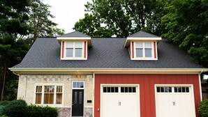 Une maison à deux étages avec un garage, une façade en briques et une porte noire.