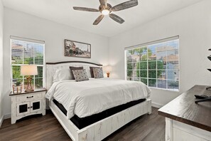 A bedroom with a bed, bedside tables, a ceiling fan, and large windows.