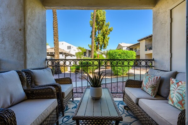 A balcony with wicker furniture, a potted plant, and a view of a residential area.