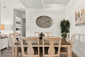 A dining area with a round table, six chairs, a vase, and a wall-mounted decorative plate.