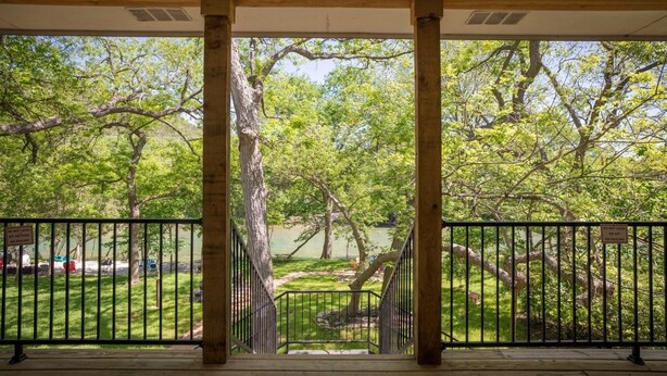 A wooden deck with a railing overlooking a park with trees and a body of water. - Hondo's River Haus Rr 1300 4 Bedroom Home by RedAwning (New Braunfels)