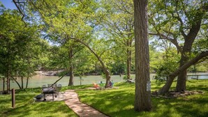 A picnic area with a grill, chairs, and a path leading to a lake. - Hondo's River Haus Rr 1300 4 Bedroom Home by RedAwning (New Braunfels)