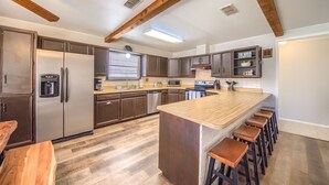 A modern kitchen with dark wood cabinets, stainless steel appliances, a central island with stools, and exposed wooden beams on the ceiling. - Hondo's River Haus Rr 1300 4 Bedroom Home by RedAwning (New Braunfels)