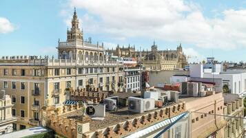 A historic building with a prominent tower and intricate architecture, surrounded by modern buildings and air conditioning units on the rooftops.