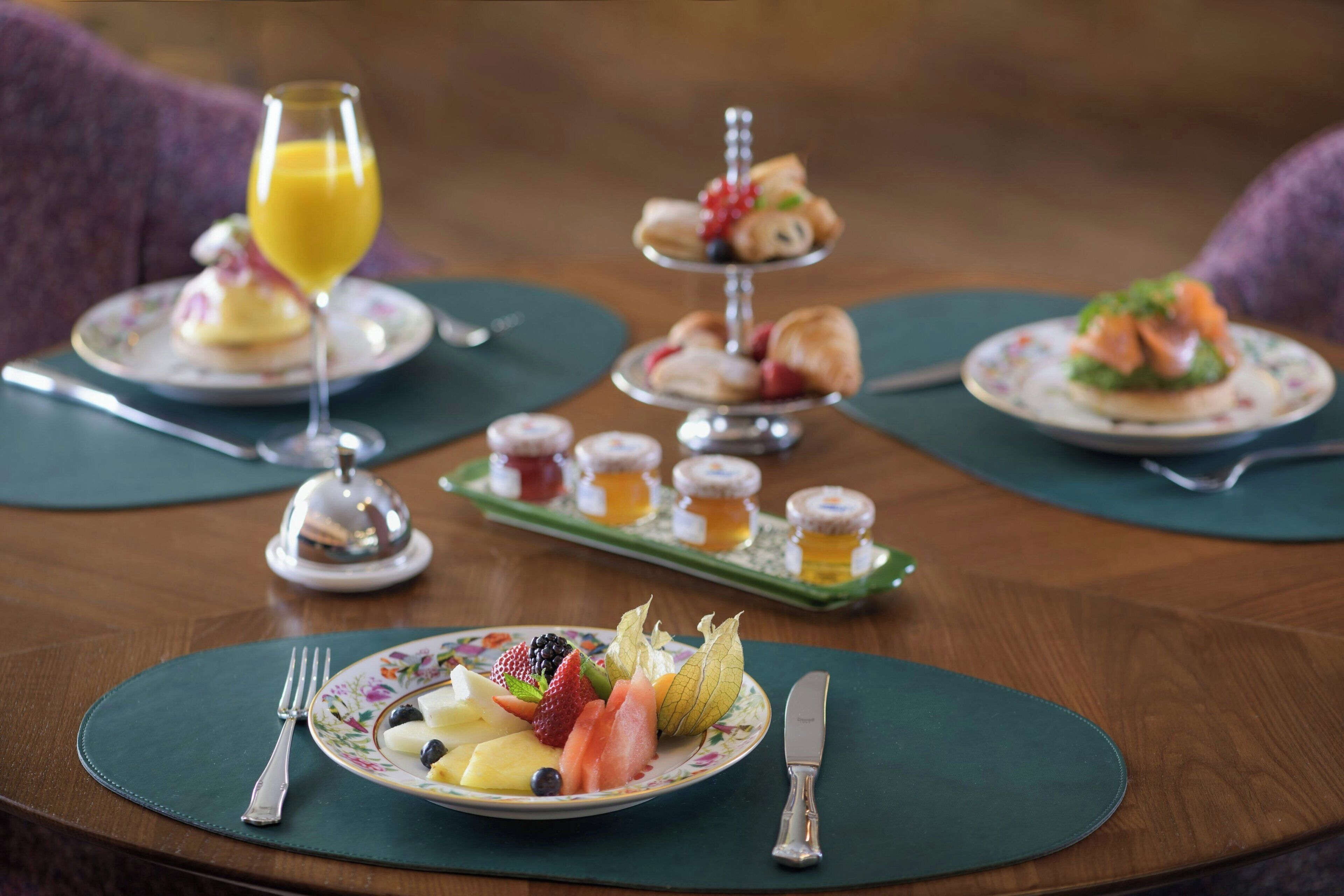 Un desayuno con diversos platos, como frutas, pastelería y un vaso de zumo de naranja.