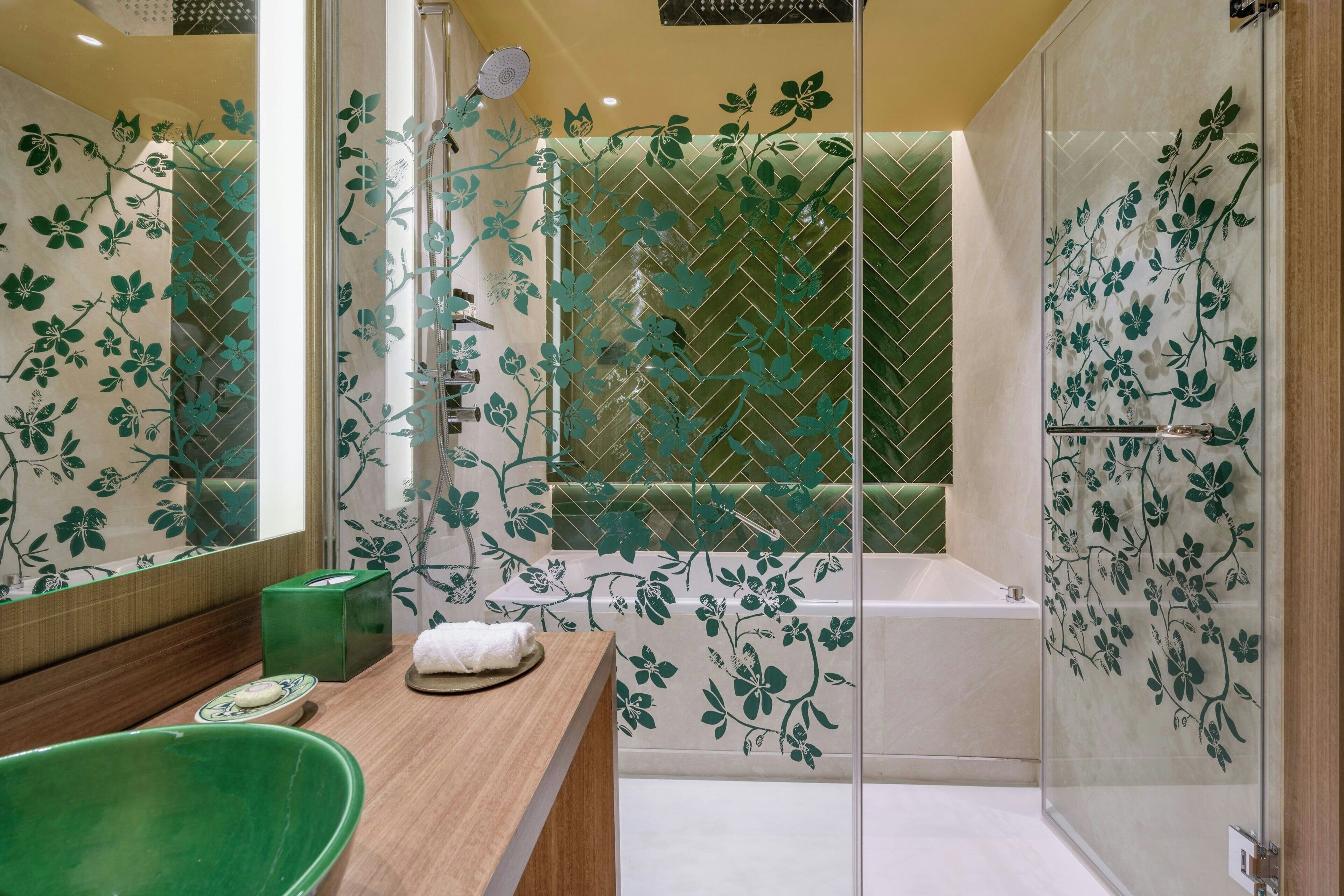 A modern bathroom with a green bathtub, a wooden vanity, a large mirror, and a glass shower enclosure with floral patterns.