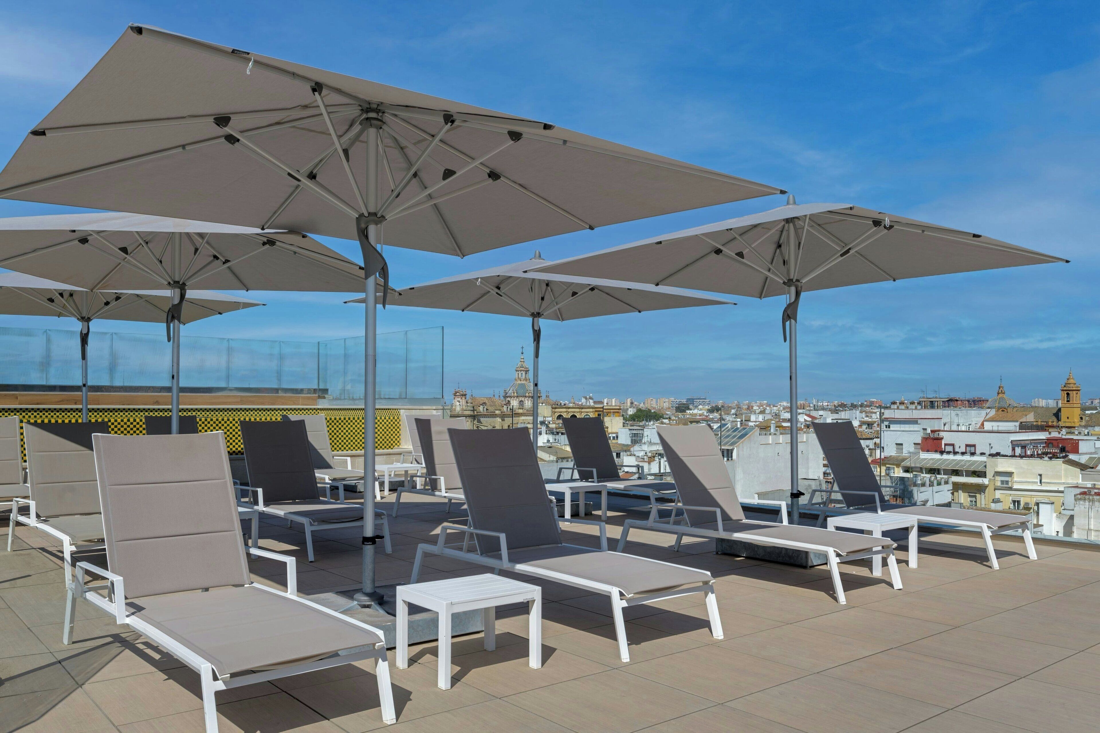 Terraza en la azotea con sillones de sol y sombrillas, con vistas a la ciudad.