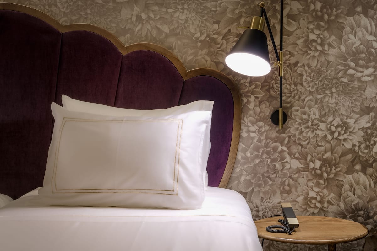 Una cama con cabecera, una mesita de noche con lámpara y un papel tapiz floral.