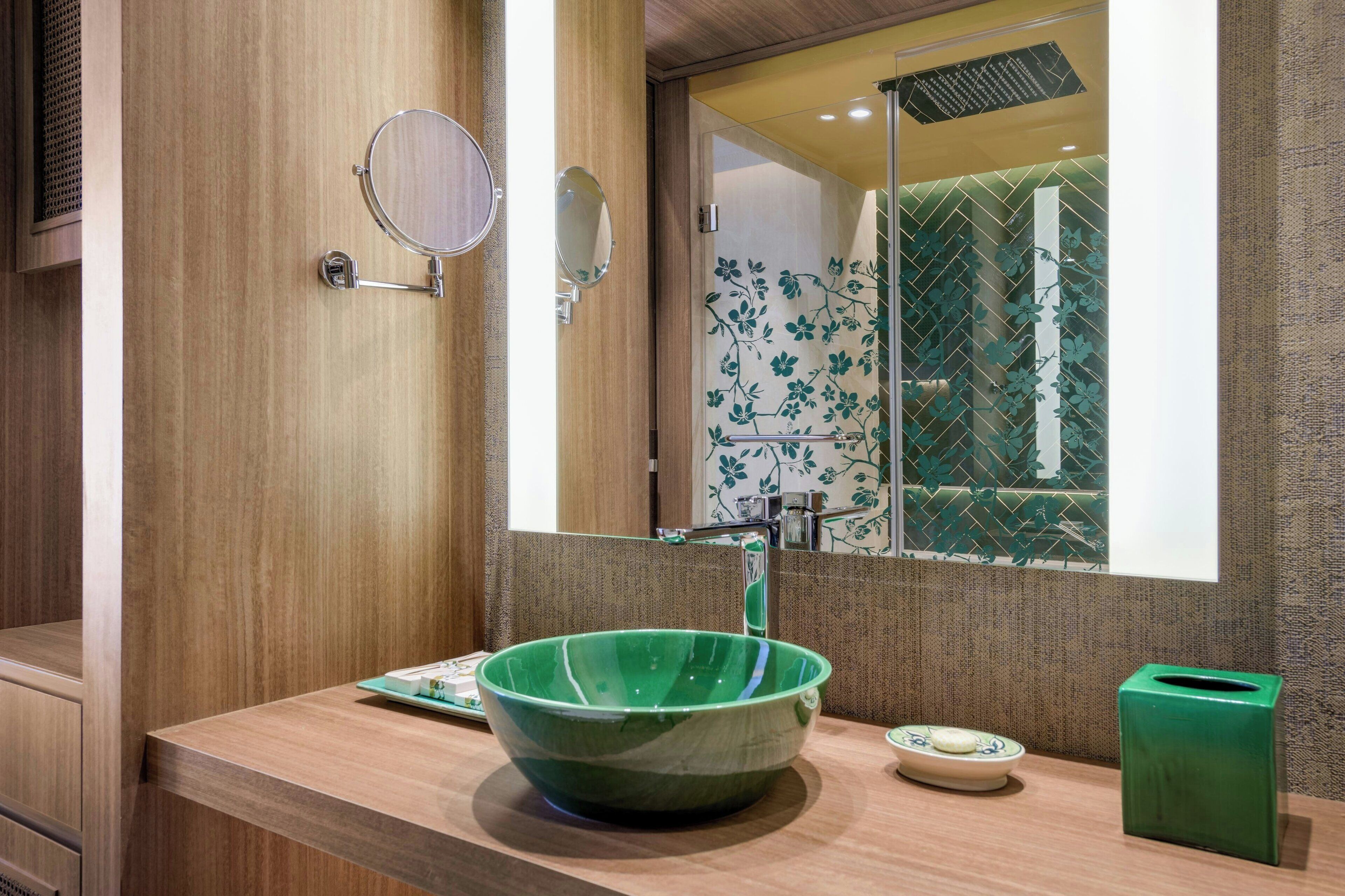Un baño con tocador de madera, lavamanos de cerámica verde, espejo y cubo de basura verde.