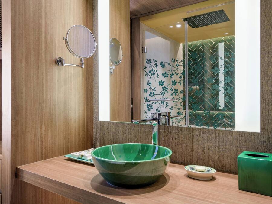 A bathroom with a wooden vanity, a green ceramic sink, a mirror, and a green trash bin.