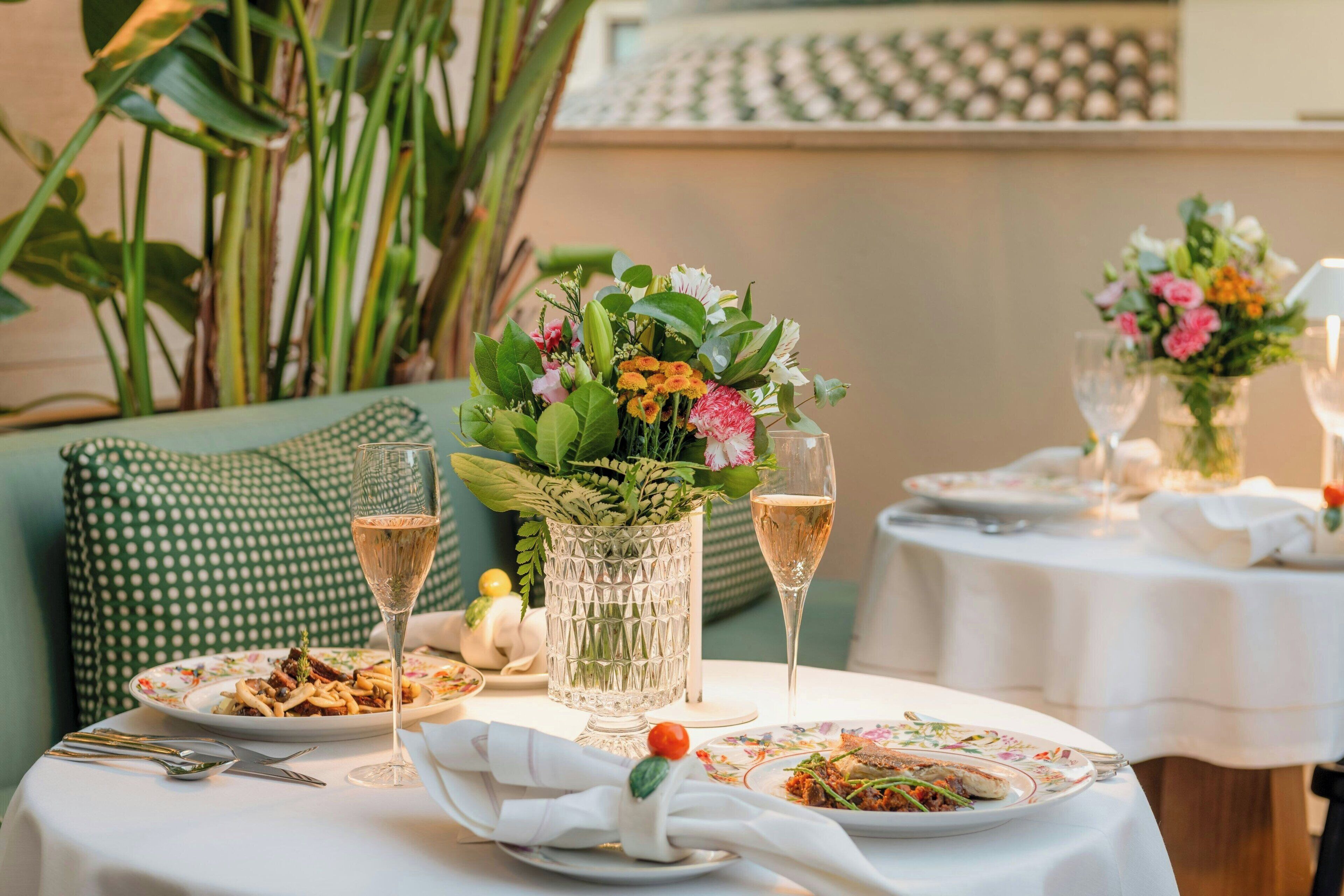 Uma mesa de jantar posta com pratos de comida, copos de vinho e um vaso de flores.