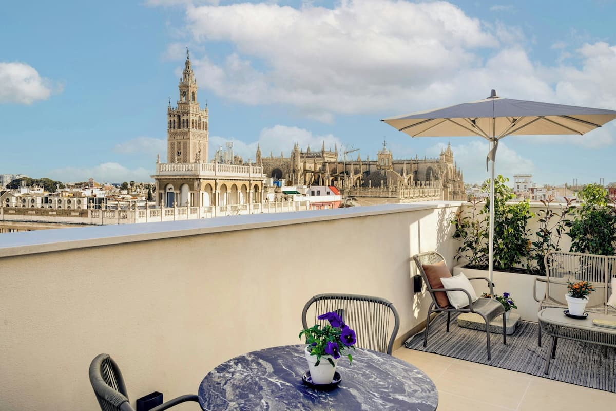 Terraza con mesa y sillas, una planta en maceta y vistas de edificios históricos, incluyendo una torre destacada.