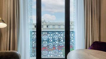 A hotel room with a large window, a view of the cityscape, and a balcony with a decorative screen.