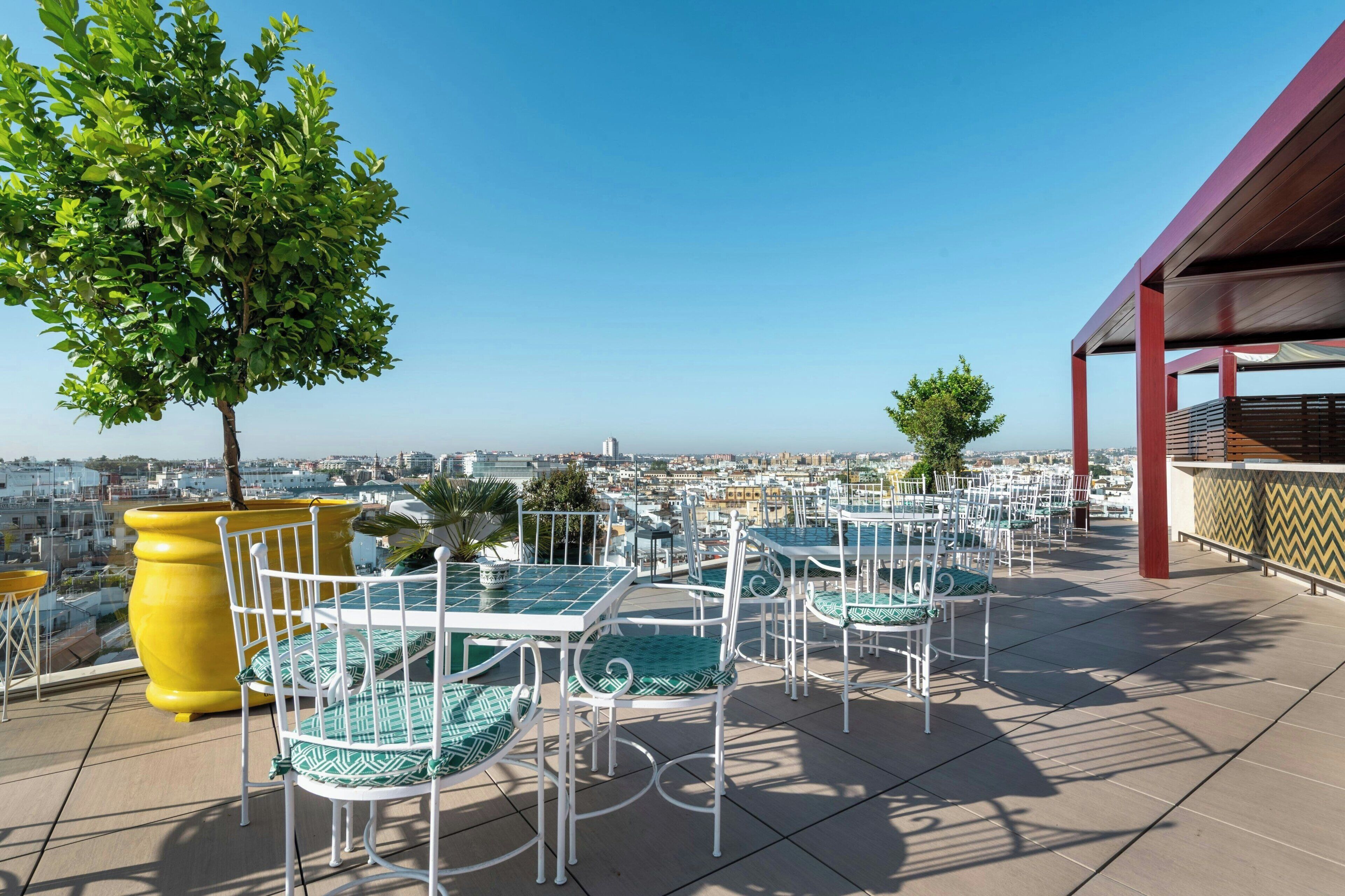 A rooftop terrace with outdoor seating, a view of the city, and a large yellow planter.