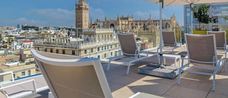 A rooftop terrace with lounge chairs and an umbrella, overlooking a historic cityscape with notable architecture.