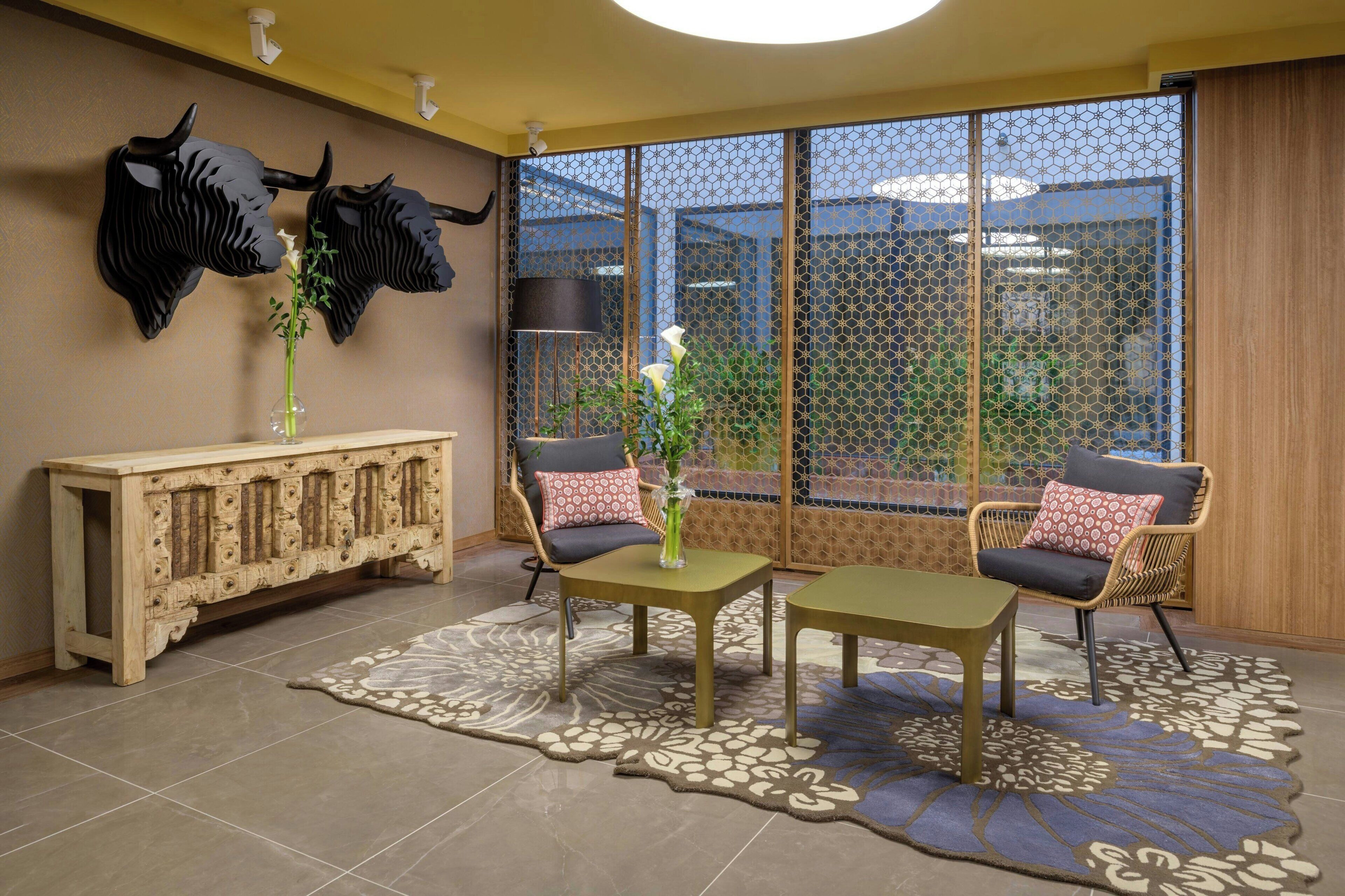 Una habitación con un ventanal grande, una consola de madera, dos sillas y una alfombra decorativa.