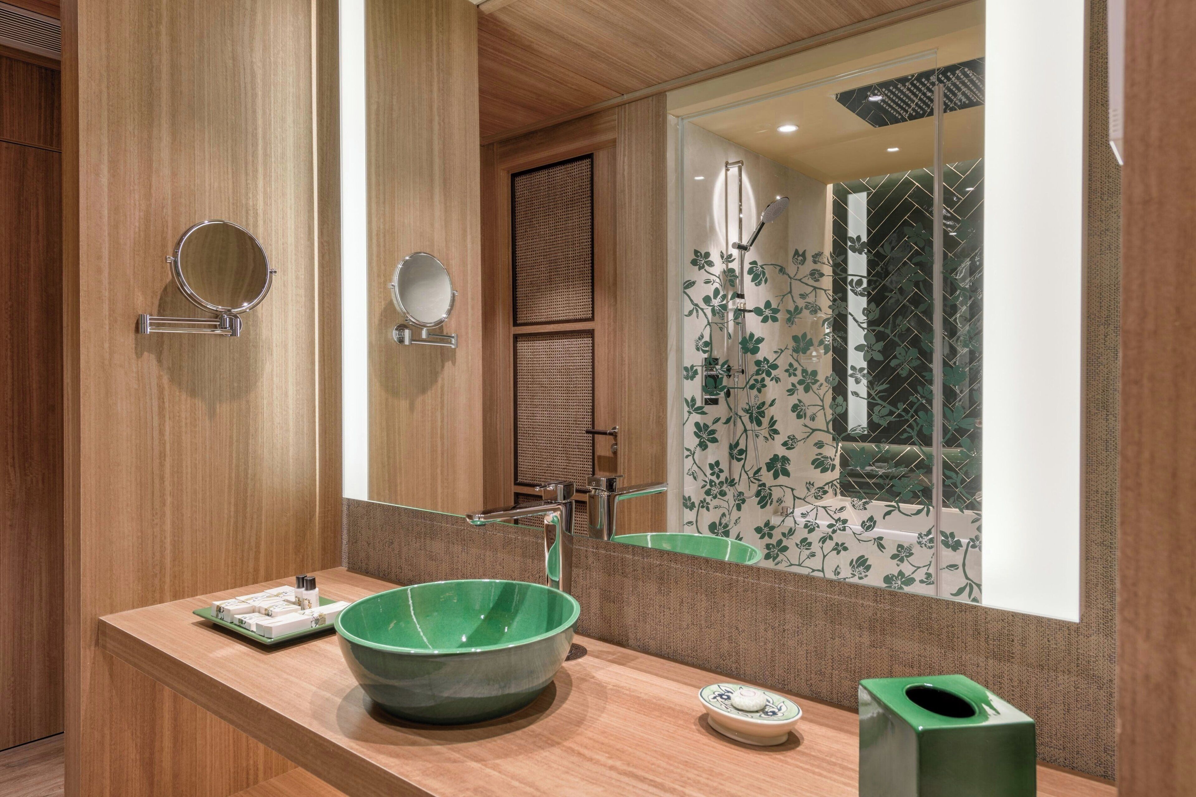 Un baño moderno con un tocador de madera, un lavabo de cerámica verde y un espejo grande.