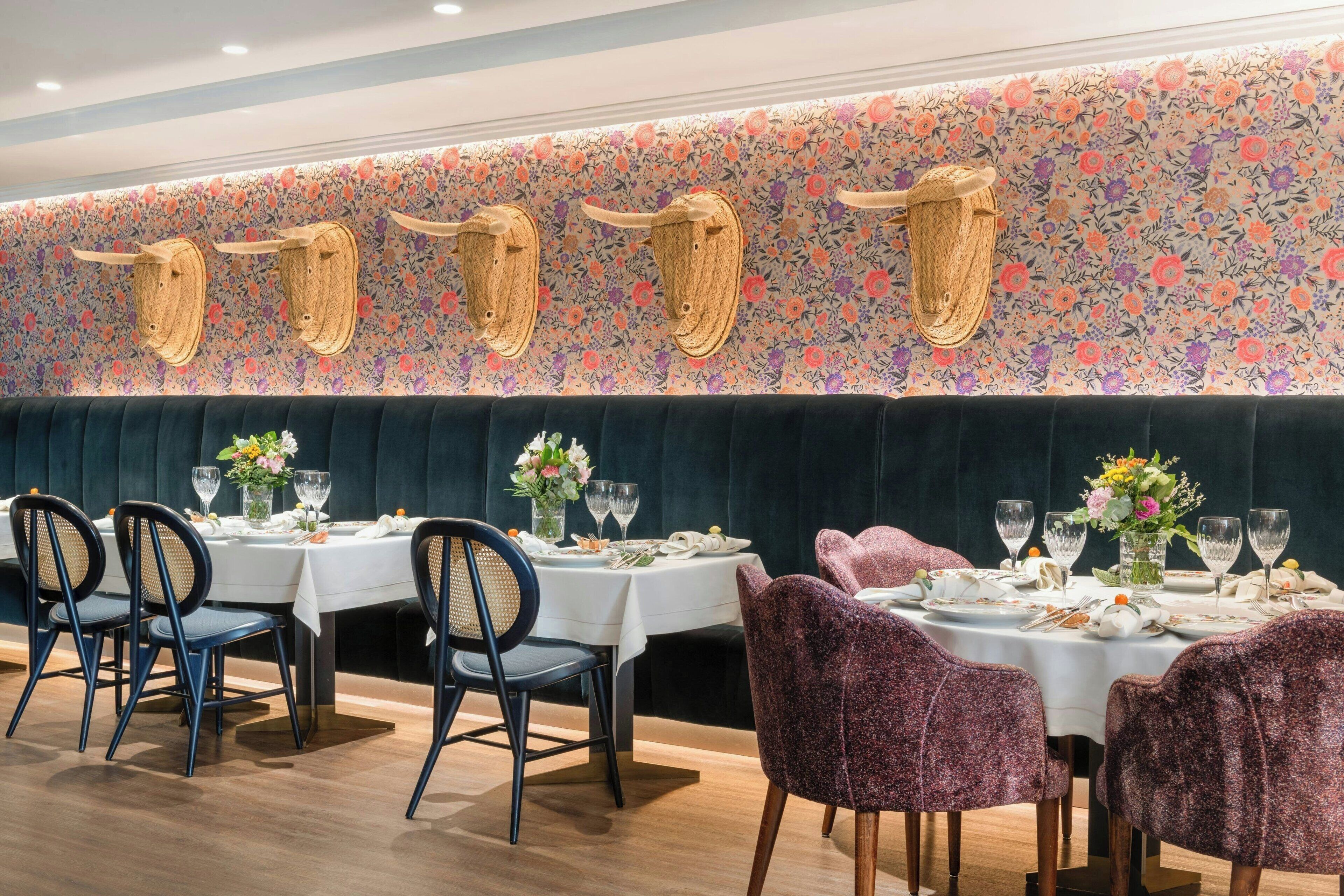 Ein Restaurant mit runden Tischen, dunkelgrünen gepolsterten Sitzbänken und dekorativen Wandleuchtern in Form von Tierhörnern.