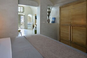 Een hotelkamer met een bed, een houten garderobe, een vaas met planten en uitzicht op het buiten.