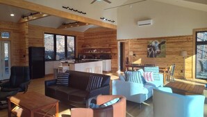 Uma sala de estar ampla com cozinha moderna, paredes de madeira e janelas grandes.