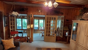 Ein gemütliches Blockhaus-Interieur mit Holzbalkendecke, Deckenventilator, einer Couch mit gemustertem Kissen, einem Schrank und einem Teppich.