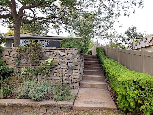 A stone staircase leading to a house with a wooden fence and greenery around.
