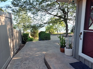 A stone pathway leading to a house with a red door, surrounded by trees and a view of the water.
