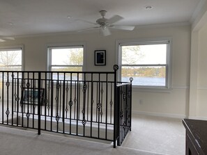 Enjoy a serene view of the water and trees from the large windows in this room, which features a ceiling fan and a dark bench.