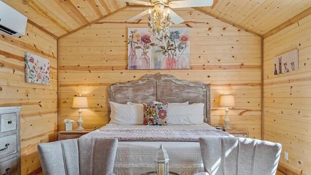 Een gezellige houten kamer met een bed, twee bedlampen, een kroonluchter en een tafeltje met een lantaarn.