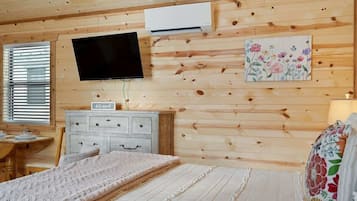 A wooden-paneled room with a bed, a dresser, a television, and an air conditioning unit.
