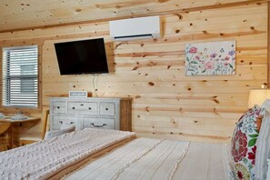 A wooden-paneled room with a bed, a dresser, a television, and an air conditioning unit.