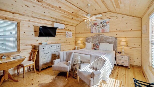 A cozy log cabin bedroom with a bed, a desk, and a chair. - Romantic Stay Right On Main St! (Fredericksburg)