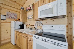 Una cocina compacta con paredes de madera, un microondas blanco, una estufa y un lavabo.