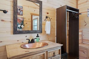 A wooden cabin bathroom with a copper sink, a mirror, a towel rack, and a wooden door. - Gorgeous Cabin on Main Street! (Fredericksburg)