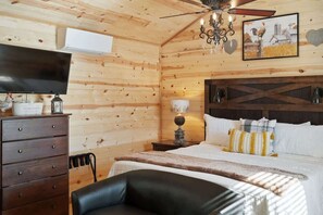 A wooden room with a bed, a TV, a dresser, and a ceiling fan. - Gorgeous Cabin on Main Street! (Fredericksburg)