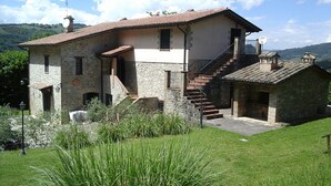 Un bâtiment en pierre avec un toit en tuiles, un escalier menant à un deuxième étage et une petite construction attenante.