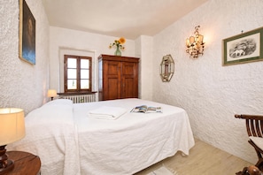 A bedroom with a bed, a wooden wardrobe, a radiator, a window, and a wall-mounted light fixture. - Il Fortino (Monteriggioni)