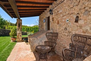 Ein überdachter Patio-Bereich mit Korbmöbeln, Steinmauern und Blick auf einen Weinberg.
