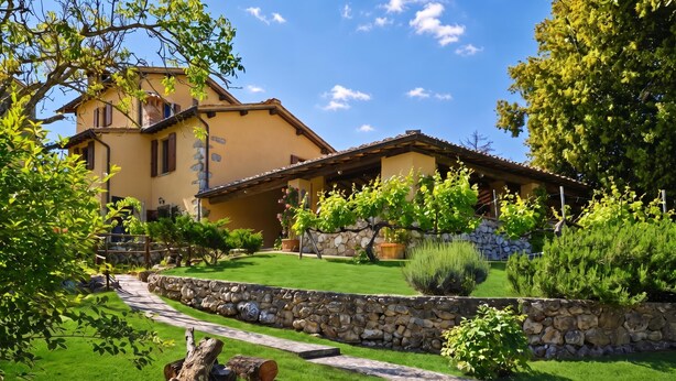 A two-story house with a stone retaining wall, a stone staircase, and a well-maintained lawn.