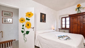 A bedroom with a bed, a door with a sunflower painting, a wooden cabinet, and a window.