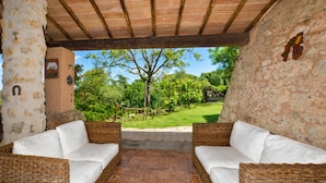 A covered patio with wicker furniture and a view of a garden.