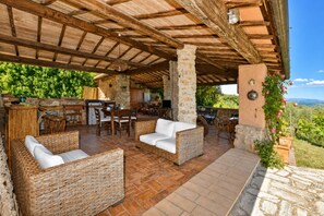 An outdoor patio with wicker furniture, stone pillars, and a view of the countryside. - Il Fortino (Monteriggioni)