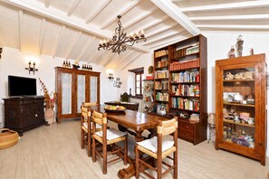 Ein Essbereich mit einem Holztisch, Stühlen, einem Fernseher und einem Bücherregal voller Bücher.