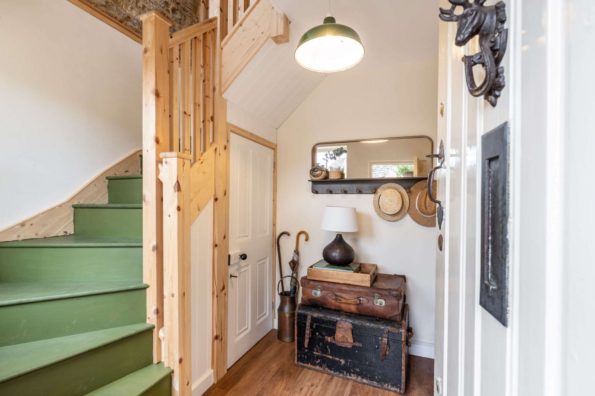 A staircase with green steps leading to a white door, a wall-mounted mirror, and a shelf with hats.